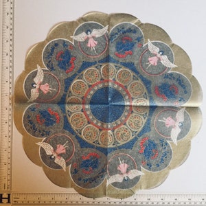 May include: A decorative paper doily with a scalloped edge. The design features a central blue circle with a red border, surrounded by blue circles with red and gold accents. Small pink angels are interspersed throughout the design, with a gold border.