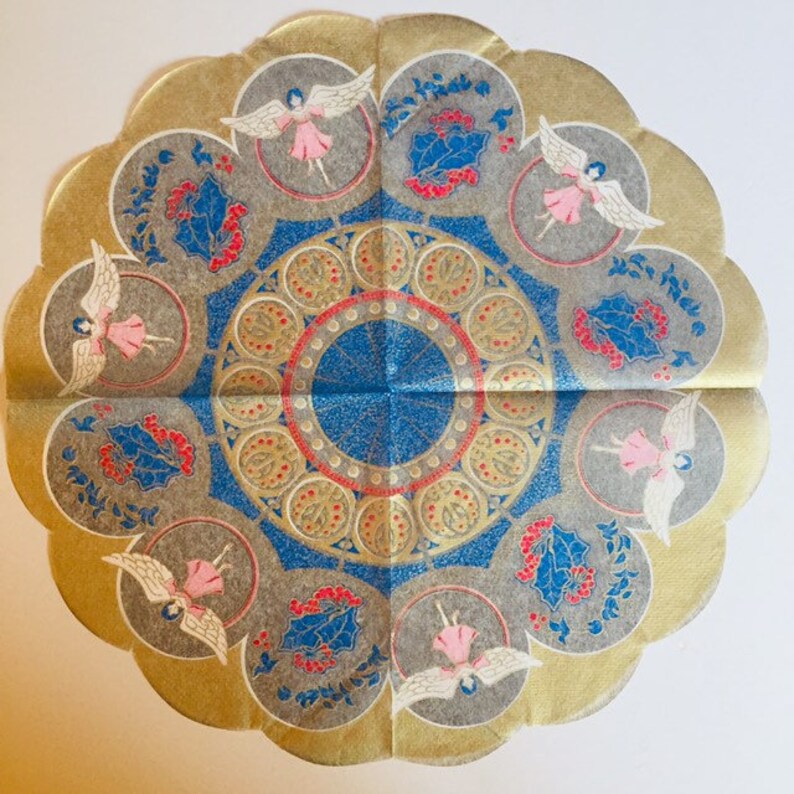 May include: A decorative paper doily with a scalloped edge, featuring a central blue and gold design. The doily is adorned with angels in pink dresses and holly sprigs, with a gold border. The overall theme is festive and holiday-oriented.