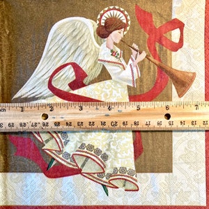 May include: A white angel with gold wings and a red ribbon plays a golden trumpet. The angel is wearing a white dress with gold and brown trim. The background is a brown and gold patterned fabric.