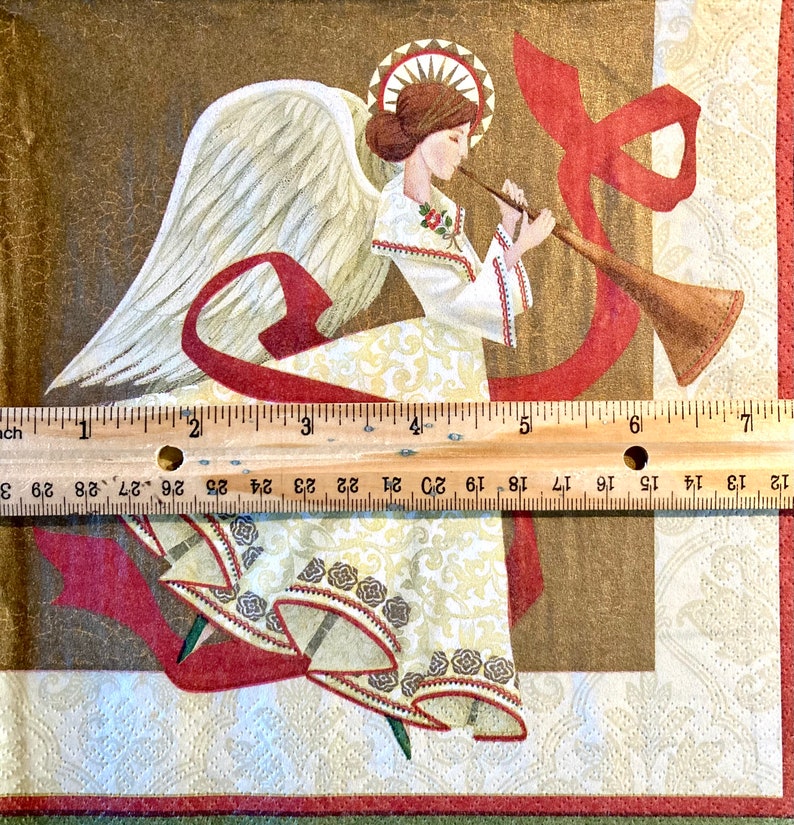 May include: A white angel with gold wings and a red ribbon plays a golden trumpet. The angel is wearing a white dress with gold and brown trim. The background is a brown and gold patterned fabric.