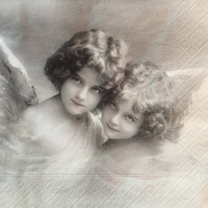 May include: A sepia-toned image of two cherubic figures with curly hair and soft features. The image is printed on a textured, off-white paper napkin, suggesting a vintage or antique aesthetic. The figures are looking towards the viewer.