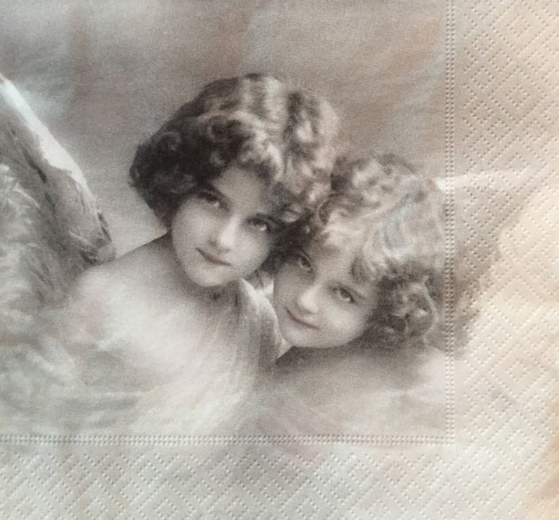 May include: A sepia-toned image of two cherubic figures with curly hair and soft features. The image is printed on a textured, off-white paper napkin, suggesting a vintage or antique aesthetic. The figures are looking towards the viewer.