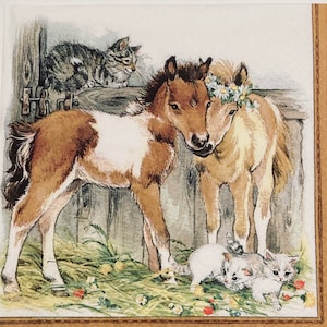 May include: Two brown and white foals with a flower crown on one of their heads stand together in a barn. A tabby cat sits on a wooden beam above them. Two white kittens are in the foreground.