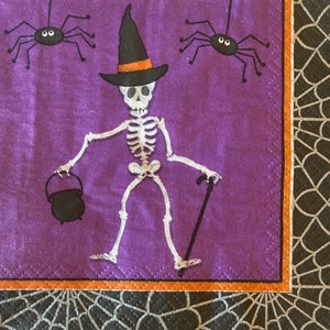 May include: A purple background with a skeleton wearing a black witch hat and holding a cauldron and a walking stick. Two black spiders with white eyes are on either side of the skeleton.
