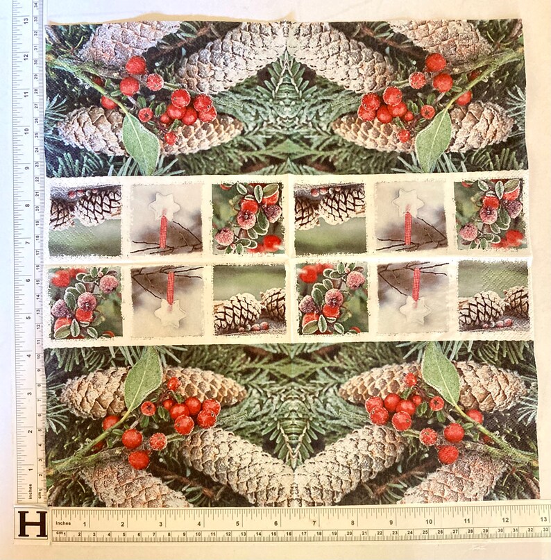 Op de afbeelding: Een witte stof met een herhalend patroon van dennenappels, hulstbesjes en groenblijvende takken. De stof heeft een vintage uitstraling met een verweerde rand rond elk beeld.