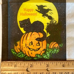 May include: A black cat sits on top of a jack-o'-lantern with a witch flying in the background. The moon is yellow and the background is black with white stars. The text "Happy Halloween!" is written in orange.
