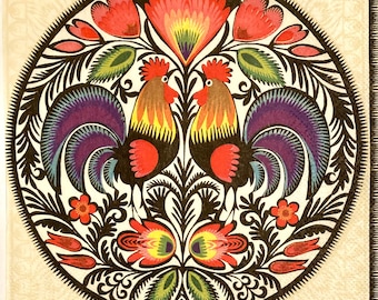 May include: A circular design featuring two stylized roosters with red, yellow, and purple plumage. The roosters are surrounded by black, green, and red floral motifs.