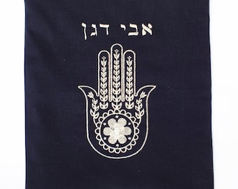 May include: A dark blue fabric pouch with a zipper closure. The pouch features a gold embroidered Hamsa hand with the Hebrew word "Hamsa" above it.