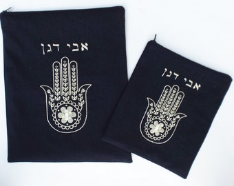 May include: Two black fabric pouches with a zipper closure. The pouches feature an embroidered silver Hamsa hand with the Hebrew text "Chai" above it.