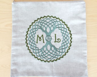 May include: A white linen tote bag with a green and blue embroidered Celtic knot design. The design features a tree of life with the initials "M & L" in the center.