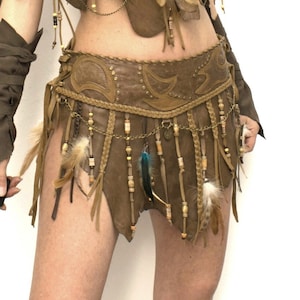 May include: A brown leather skirt with fringe and feathers. The skirt has a beaded belt with a chain and metal accents.