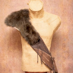 Op de afbeelding: Een bruinleren koker met een schoudervulling van bont, tentoongesteld op een mannequin. De koker is gemaakt van meerdere aan elkaar gestikte leren stukken. Het bont is donkergrijs.