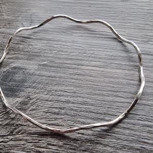 May include: A silver bangle bracelet with a wavy, textured design.