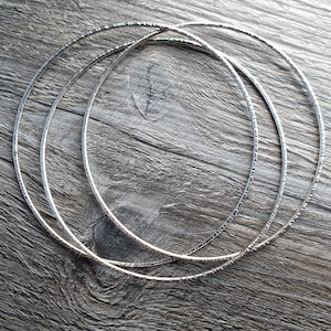 Könnte beinhalten: Drei silberne Metallreifen mit einer strukturierten Oberfläche. Die Reifen sind übereinander gestapelt.