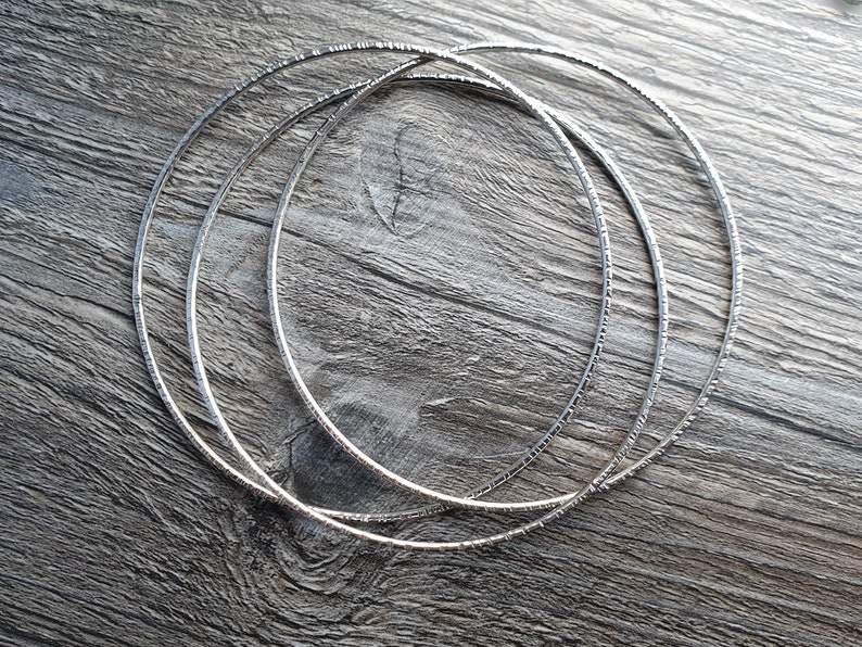 K&ouml;nnte beinhalten: Drei silberne Metallreifen mit einer strukturierten Oberfl&auml;che. Die Reifen sind &uuml;bereinander gestapelt.