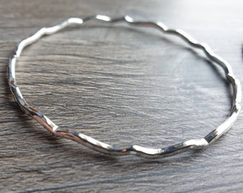 May include: A silver bangle bracelet with a wavy, hammered design.