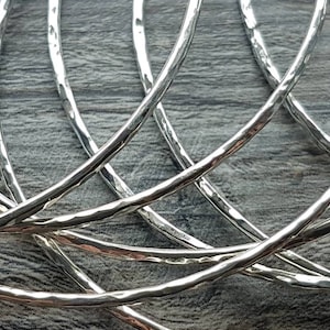 May include: A set of five silver hammered bangle bracelets. The bracelets are stacked on top of each other, showing the hammered texture.