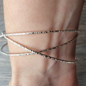 K&ouml;nnte beinhalten: Ein silbernes Armband mit strukturiertem Design. Das Armband besteht aus drei d&uuml;nnen B&auml;ndern, die miteinander verwoben sind.