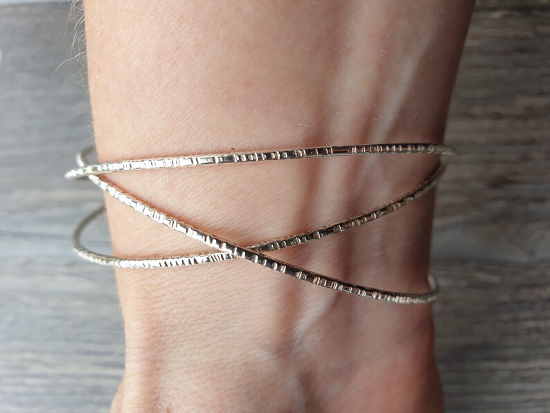 K&ouml;nnte beinhalten: Ein silbernes Armband mit strukturiertem Design. Das Armband besteht aus drei d&uuml;nnen B&auml;ndern, die miteinander verwoben sind.