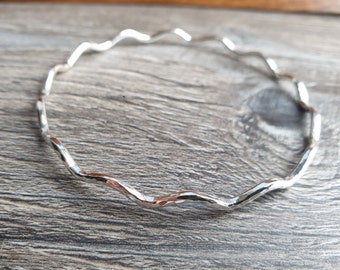 May include: A silver bangle bracelet with a wavy, textured design.