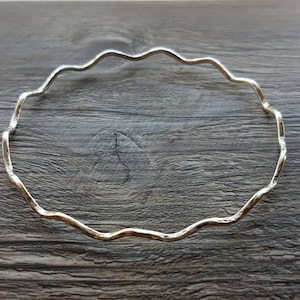 May include: A silver bangle bracelet with a wavy, textured design.