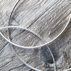 K&ouml;nnte beinhalten: Drei silberne Metallreifen mit strukturierter Oberfl&auml;che, auf einem Holzmaserungshintergrund angeordnet.