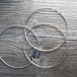 K&ouml;nnte beinhalten: Drei silberne Metallreifen in verschiedenen Gr&ouml;&szlig;en, &uuml;bereinander gestapelt auf einer Holzoberfl&auml;che.