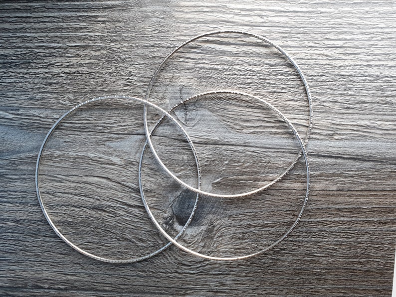 K&ouml;nnte beinhalten: Drei silberne Metallreifen in verschiedenen Gr&ouml;&szlig;en, &uuml;bereinander gestapelt auf einer Holzoberfl&auml;che.