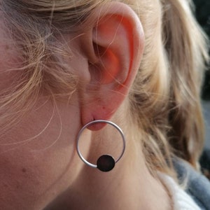 May include: Silver hoop earrings with a black circle pendant.