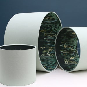 May include: Three lampshades with a light green fabric exterior. The largest lampshade has a black and green floral print on the inside. The two smaller lampshades have a solid light green interior.