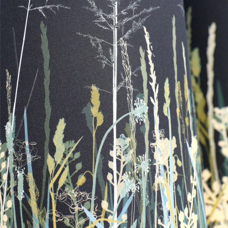K&ouml;nnte beinhalten: Schwarzer Stoff mit einem wei&szlig;en und gr&uuml;nen Blumenmuster. Das Muster zeigt hohes Gras und Blumen.