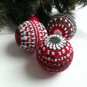 May include: Three crocheted Christmas ornaments in red, white, and green. The ornaments are round and have a textured surface.