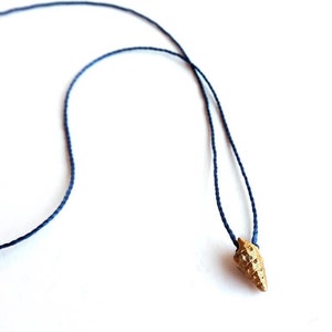 Puede incluir: Un collar con un colgante de concha dorada en un cordón azul oscuro.
