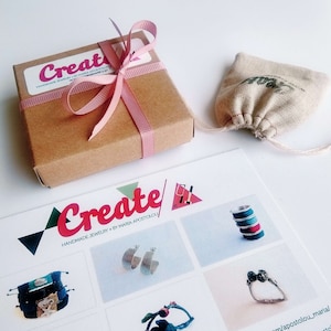 May include: A brown cardboard box tied with a pink ribbon, a small drawstring bag, and a brochure featuring the word "Create" in pink and red. The brochure showcases handmade jewellery.
