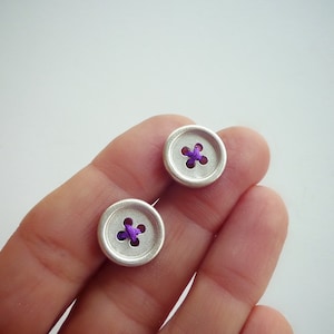 Op de afbeelding: Twee zilveren knoop-oorbellen met paarse draadaccenten.