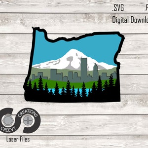 May include: A digital download featuring an Oregon state outline with a scenic landscape. The design includes a mountain, skyline, trees, and a lake, all in a silhouette style. The text reads '.SVG .PDF Digital Download'. The logo for Creevy Creations is also present.