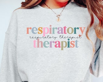 May include: A gray sweatshirt with the text "respiratory therapist" in colorful letters. The text is in a rainbow color scheme.