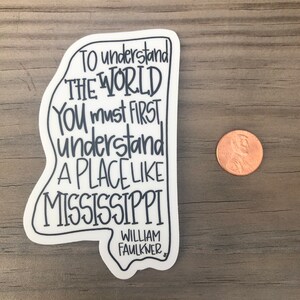 May include: White sticker with a black outline of the state of Mississippi. The sticker features a quote by William Faulkner: "To understand the world you must first understand a place like Mississippi."