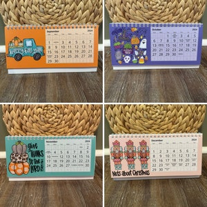 May include: Four seasonal desk calendars for 2024. Each calendar features a different theme: fall, Halloween, Thanksgiving, and Christmas. The calendars have a spiral binding and include the month's days.