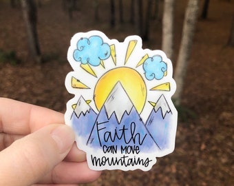 May include: A sticker with a watercolor illustration of a sun rising over mountains. The text "Faith can move mountains" is written in a handwritten font.