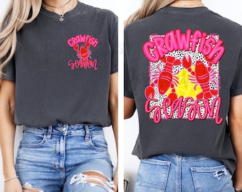 May include: A gray t-shirt with a pink and red crawfish design on the front and back. The front design says "Crawfish Season" and the back design says "Crawfish Season" with two crawfish and a yellow star.