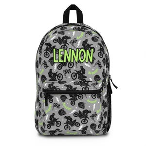 May include: A gray backpack featuring a repeating pattern of black dirt bikes, helmets, checkered flags, lightning bolts, and the green text "Braaap". The name "LENNON" is printed in large, lime green capital letters across the center front.