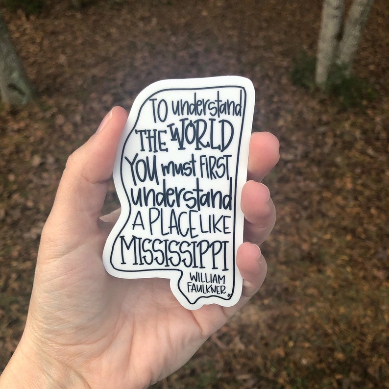 May include: A white sticker shaped like the state of Mississippi with a black outline. The sticker features a quote by William Faulkner: "To understand the world you must first understand a place like Mississippi."