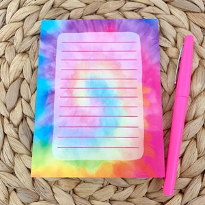 May include: A tie-dye notepad with a white lined rectangle in the center. The notepad has a rainbow tie-dye pattern with pink, blue, yellow, and orange colors.