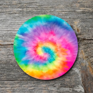 May include: A round coaster with a vibrant tie-dye design. The coaster features a spiral pattern of bright colors including pink, yellow, green, blue, and purple. The coaster is set against a rustic, weathered wood background.