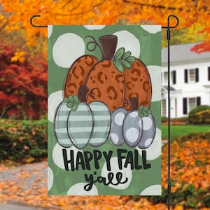 May include: A garden flag featuring a fall-themed design. The flag displays a collection of pumpkins in shades of orange, gray, and blue, with a green background and white polka dots. The text "HAPPY FALL y'all" is prominently displayed.