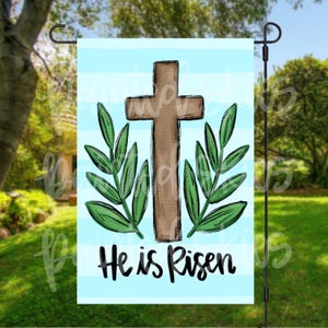 May include: A blue and white striped garden flag with a brown wooden cross and green leaves. The text "He is Risen" is written in black below the cross.