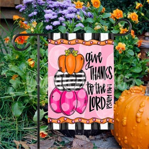 May include: A pink and black striped garden flag with a stack of pumpkins and the text "give THANKS to the LORD PSALM 136:1".