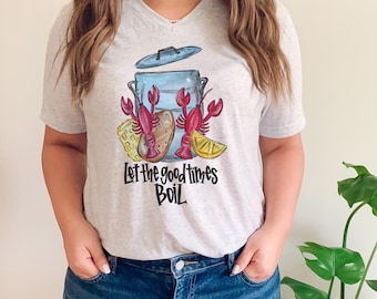 May include: A gray V-neck t-shirt with a graphic of a pot of crawfish, corn, potatoes, and lemons. The text "Let the good times boil" is printed below the pot.