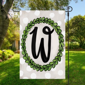 May include: A white garden flag with a green wreath and the letter W in black. The background is a white and gray polka dot pattern.